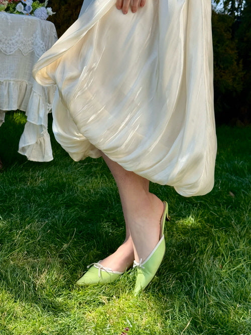 Close-up of romantic cream balloon skirt with soft satin texture, styled with pastel green ribbon heels on grass – fairytale-inspired feminine fashion detail