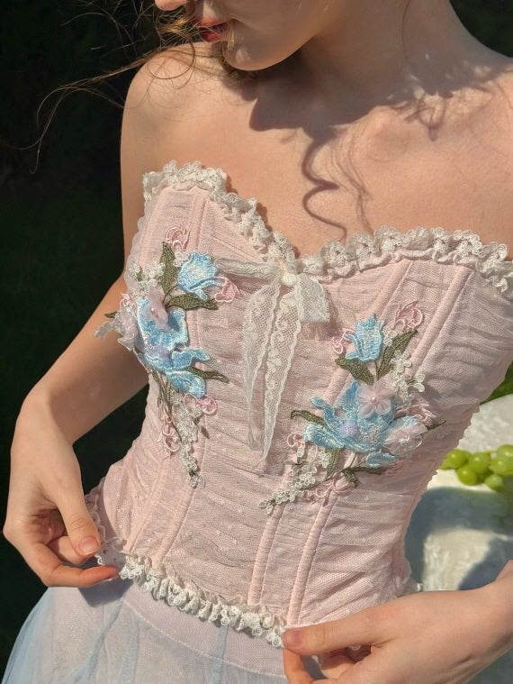 Close-up of embroidered corset bodice with delicate blue and pink floral appliqués, lace trim, and ribbon bow – vintage fairytale-inspired feminine detail