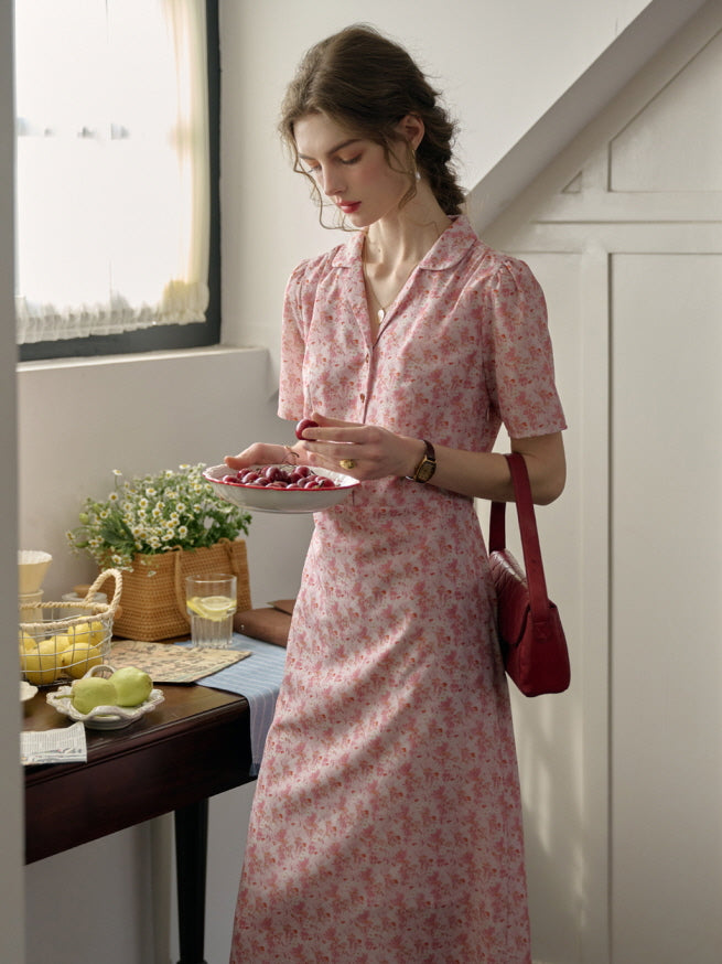 A woman in a casual cottagecore pink dress with delicate floral patterns, enjoying a quiet moment with fresh cherries in a cozy countryside-inspired interior.