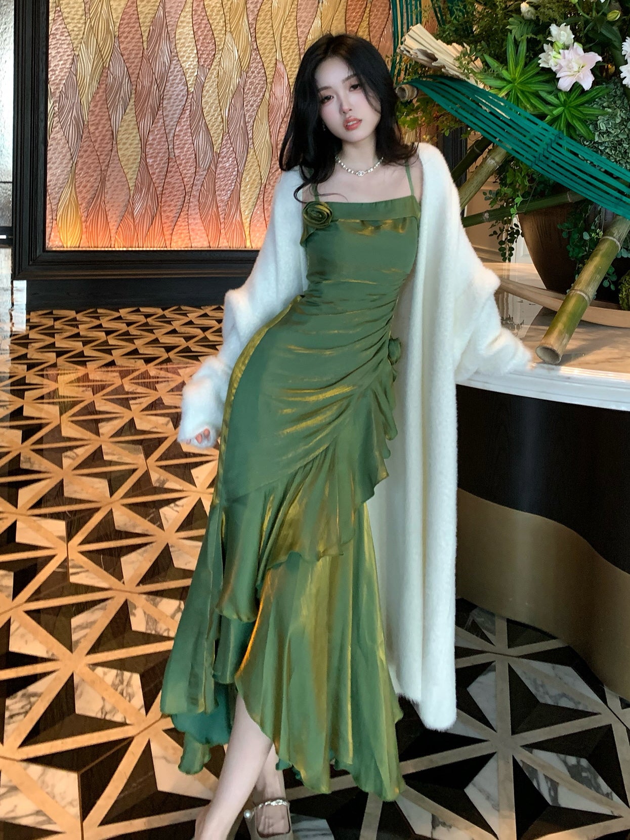Romantic ruffle dress in emerald tones, leaning on a marble counter with golden light accents.