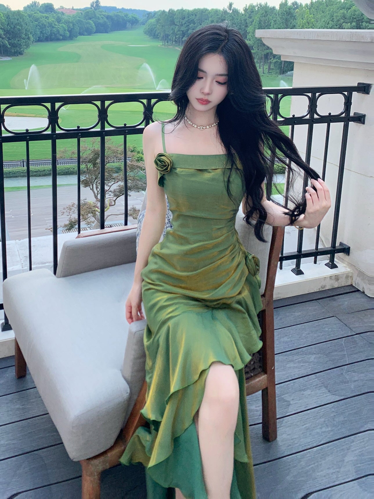 Elegant green satin dress with rose details, captured sitting in a romantic courtyard chair.