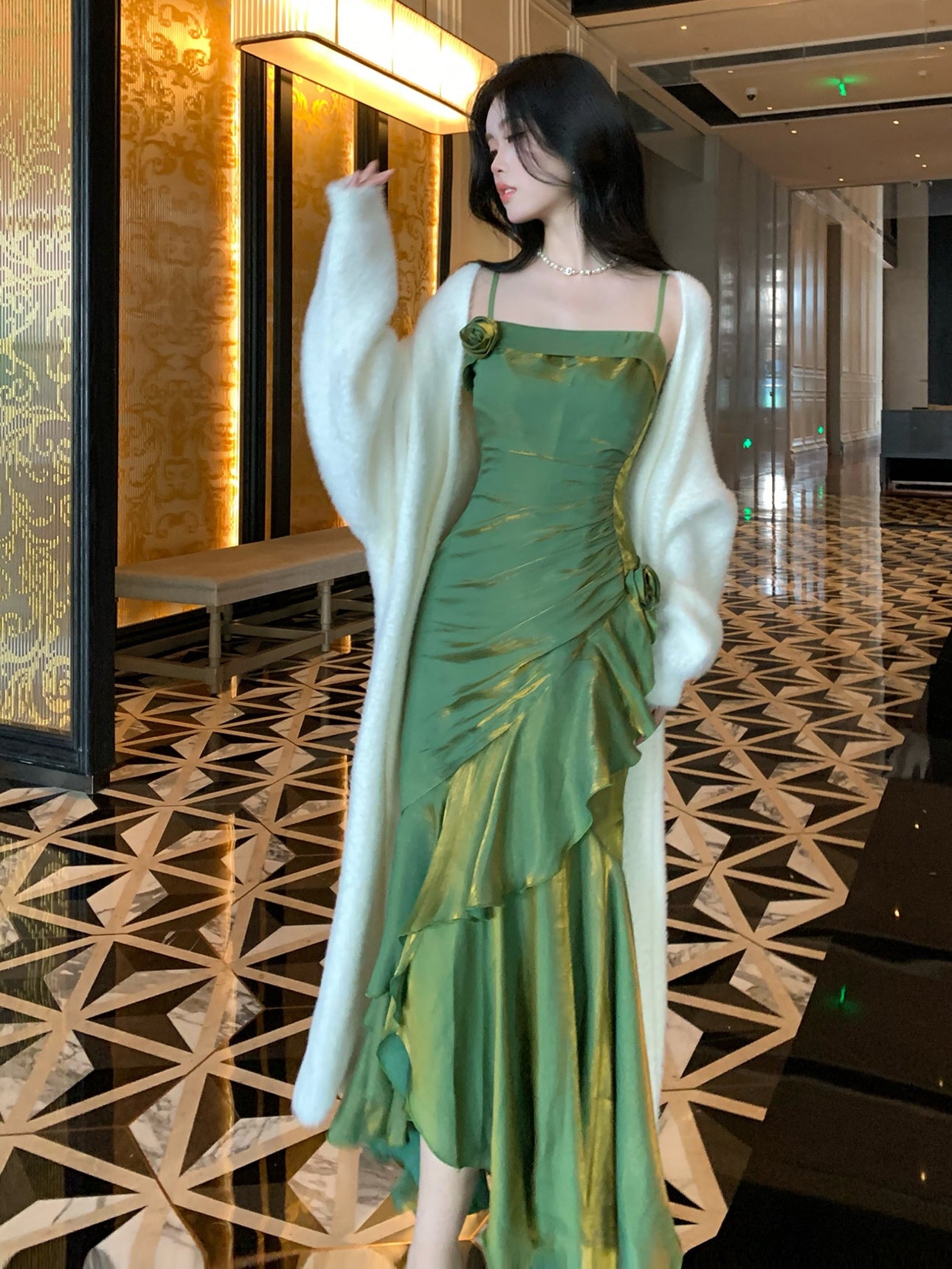 Close-up of silk-like green dress showing rose appliqué and side pleats, worn with white cardigan.