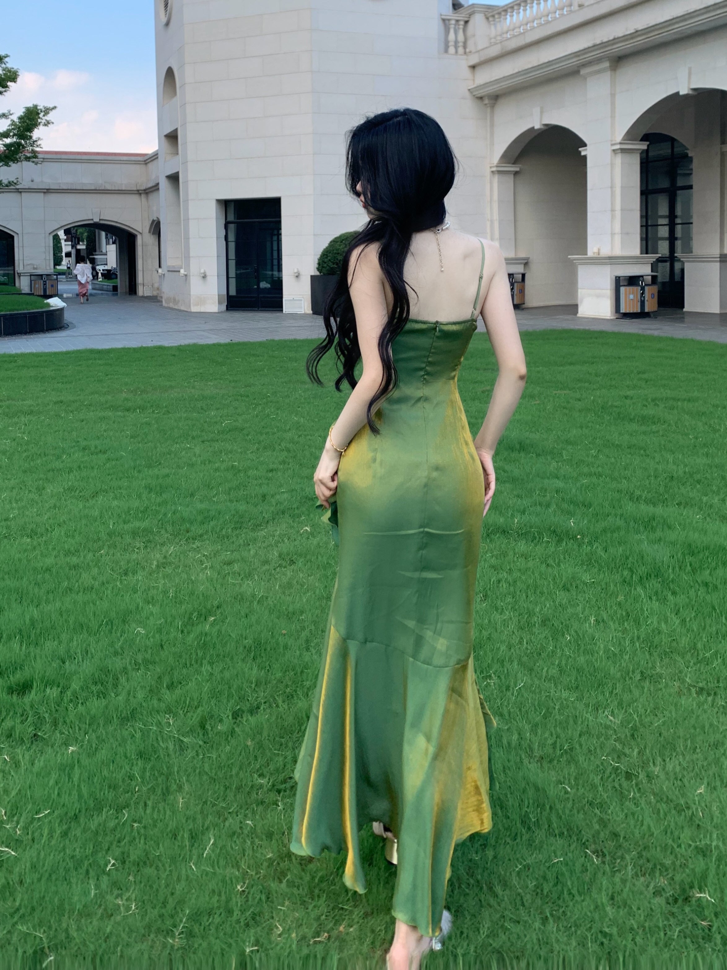 Back view of flowing green fairy princess evening dress with golden shimmer, worn in a garden scene.