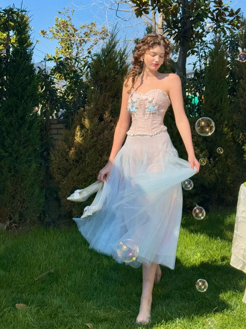 Romantic pastel blue corset dress with floral embroidery and flowing tulle skirt, worn barefoot in a garden with bubbles – whimsical fairytale-inspired outfit for women
