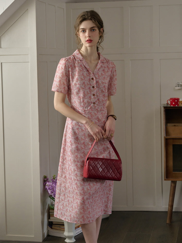 A woman in a pink floral cottagecore dress with short sleeves, styled with a casual red quilted handbag for a relaxed and charming look.