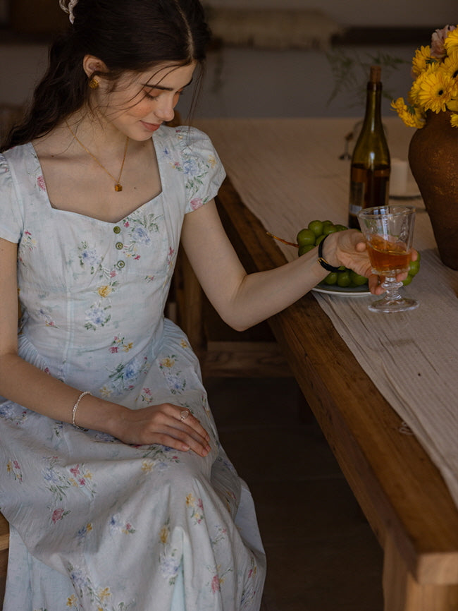 Vintage-inspired floral dress with a sweetheart neckline, delicate button-down front, and pastel flower prints, capturing a serene, fairytale-like afternoon setting with soft lighting and rustic decor.
