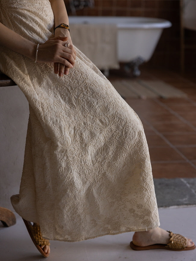 Close-up view of a cream-colored floral textured midi dress with intricate embroidery, highlighting the flowing skirt and relaxed, feminine silhouette.