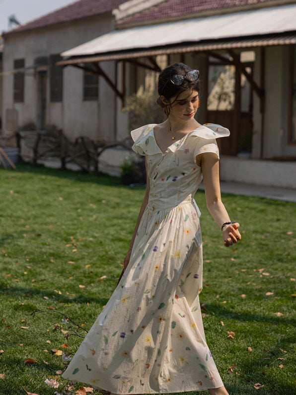 Young woman wearing a vintage floral cottagecore dress with flutter sleeves, standing in a sunlit garden with a relaxed, dreamy expression.