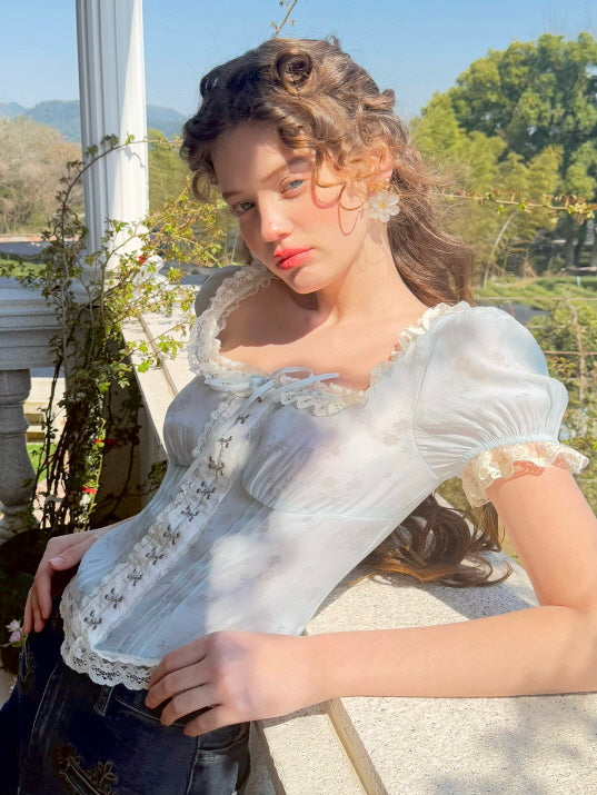 A model poses in a vintage-inspired pastel blue floral corset top paired with dark denim jeans, capturing a dreamy, fairytale look under warm natural sunlight at Romantic Fairytale store.