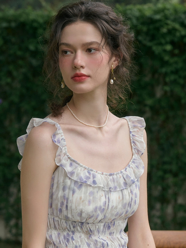 Woman with curly hair and pearl earrings wearing a vintage-inspired floral cottagecore dress with ruffle details, gazing thoughtfully in a garden.