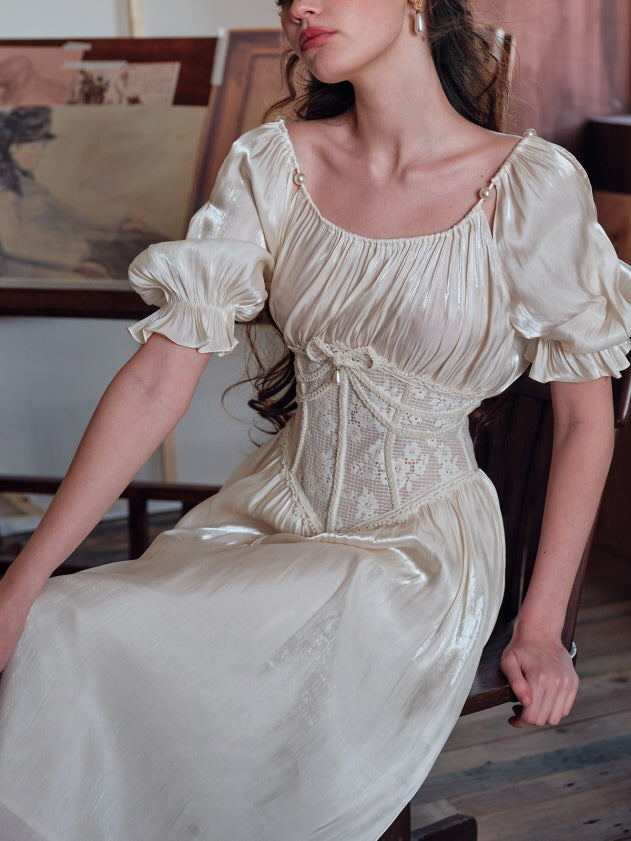 A seated woman wearing an ivory puff-sleeve dress with a pearl-accented neckline and an embroidered lace corset, exuding a graceful and artistic old-world charm.