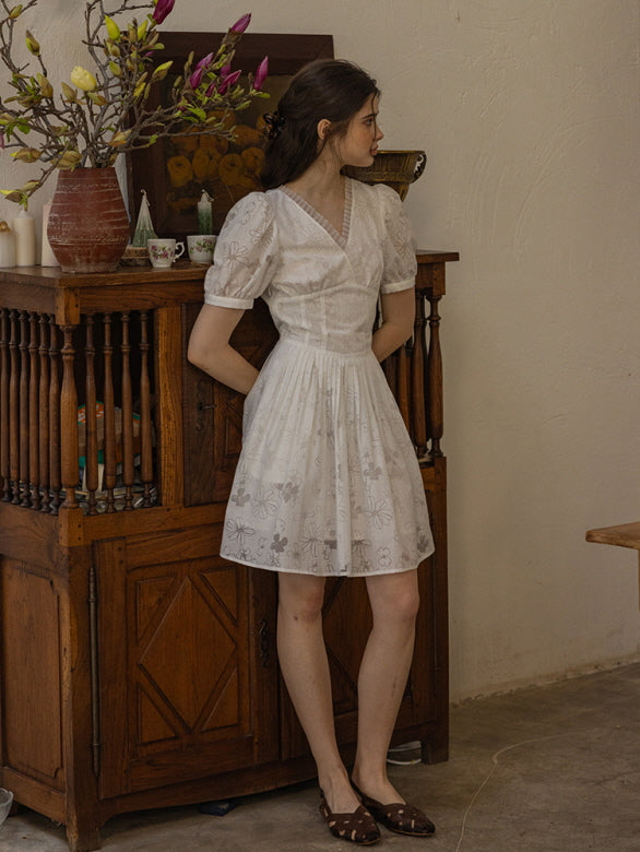 Rustic wooden cabinet with a vintage-inspired white floral mini dress featuring delicate puff sleeves and a pleated skirt, creating a romantic cottagecore aesthetic.