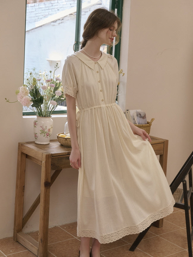 Woman in a cream-colored cottagecore vintage dress with lace hem and short sleeves, sitting gracefully by a rustic wooden table with flowers, wearing an elegant retro outfit.
