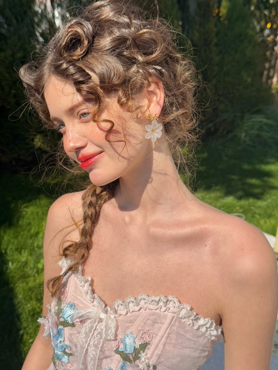 Close-up of a woman wearing a pink floral embroidered corset dress and white flower earrings, styled with vintage curls in a dreamy garden setting – romantic feminine fashion