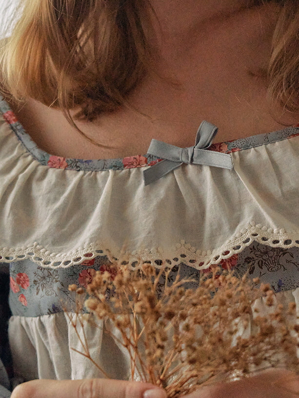 A close-up of the neckline of a blue floral nightgown, featuring a delicate lace trim and a soft satin bow for a romantic, cottagecore look.