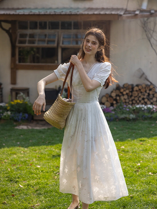 Sunlit garden scene with a woman wearing a white embroidered dress, carrying a woven straw bag, and smiling joyfully.