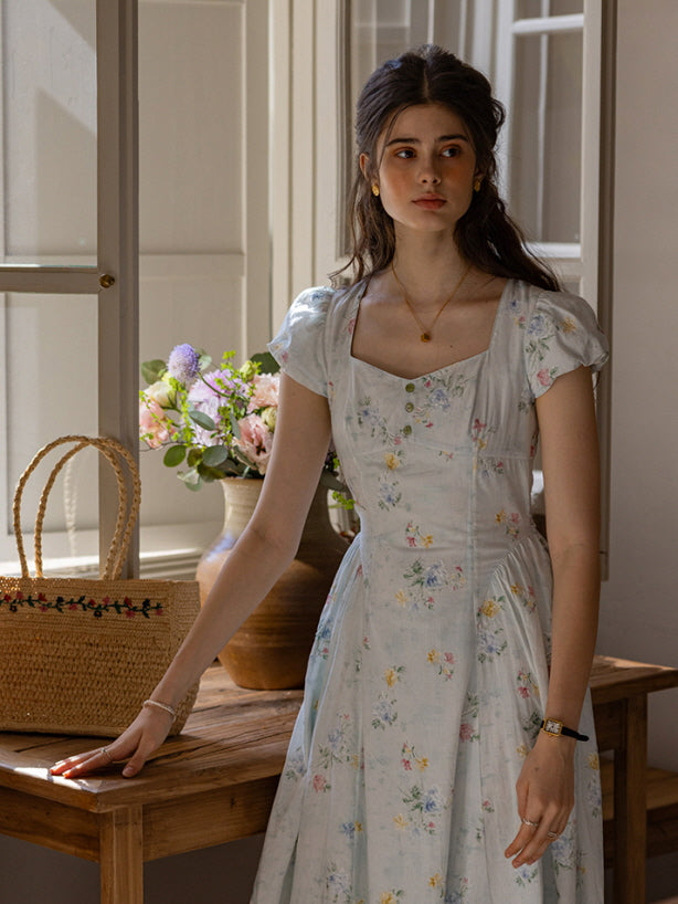 Delicate floral dress with a flattering button-down front and vintage-inspired puff sleeves, set against a rustic, cottagecore backdrop with natural light and a charming flower arrangement.