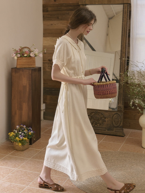 Model walking indoors wearing a cream vintage-inspired dress with lace trim and short sleeves