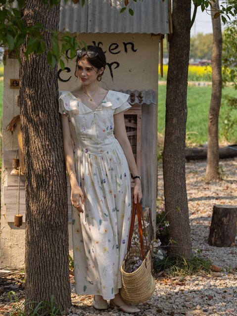 Woman leaning against a tree in a vintage-inspired floral dress with flutter sleeves, holding a straw basket filled with flowers, evoking a dreamy countryside atmosphere.