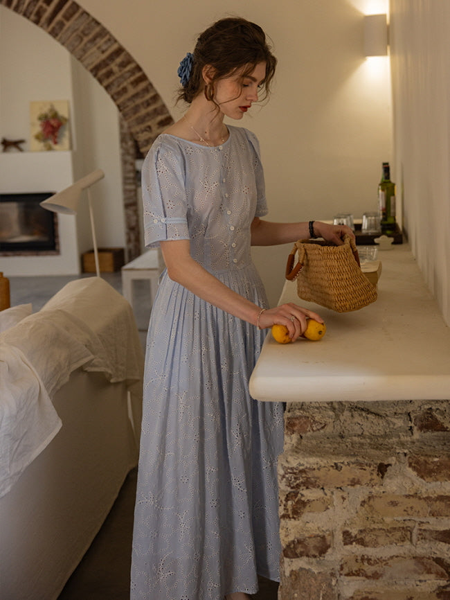 Woman arranging lemons on a stone countertop, styled in a blue eyelet lace dress with puff sleeves and a woven basket. Cozy, vintage-inspired scene.