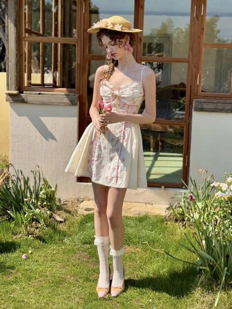 Feminine coquette mini dress with floral print, lace trim, and ribbon bow, styled with lace socks and a straw hat. Vintage-inspired summer outfit capturing a sweet, romantic garden scene.