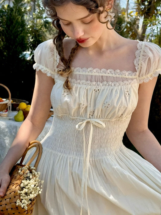 A romantic cottagecore-inspired woman wearing an ivory vintage dress with puff sleeves, lace trim, and floral eyelet embroidery, holding a woven basket of flowers in a fairytale garden setting.