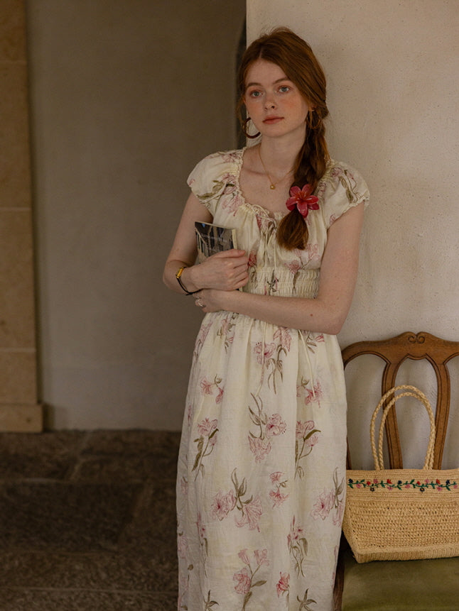 A woman leaning against a wall, holding a book while wearing a vintage-inspired floral cottagecore dress with puff sleeves and a smocked waist. Soft, dreamy aesthetic.
