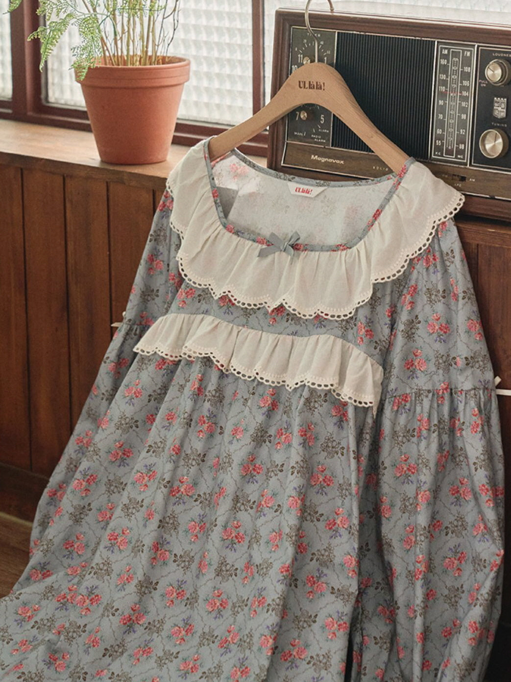 A blue floral nightgown with lace ruffle details and a satin bow, elegantly draped over a wooden hanger, exuding vintage cottagecore charm.