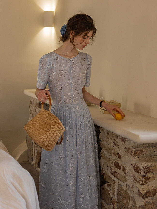 Side view of a woman holding a lemon and woven basket, styled in a blue eyelet lace dress with floral patterns. Romantic, vintage-inspired look.
