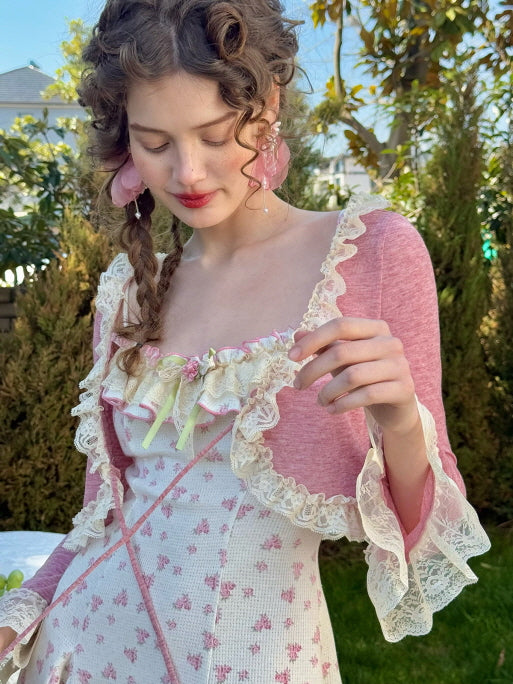 A close-up of a model wearing a romantic cottagecore dress with pink floral patterns, lace-trimmed ruffles, and a pastel pink bolero with flared lace cuffs, creating a dreamy, fairytale aesthetic.