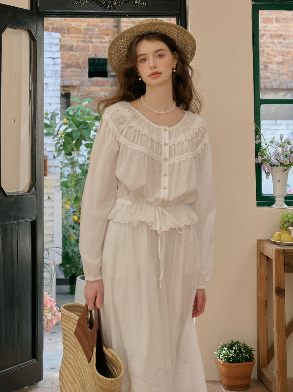 A woman wearing a white vintage-inspired cottagecore blouse and skirt set, accessorized with a straw hat and pearl necklace, standing in front of a garden doorway.