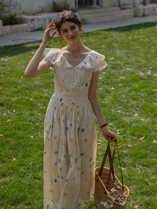 Smiling woman in a cottagecore floral dress with ruffled sleeves, adjusting her sunglasses while holding a woven basket filled with flowers in a sunlit garden.