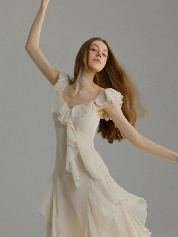 Ivory romantic dress captured in motion with raised arms, highlighting the airy ruffle neckline, flowing chiffon layers, and elegant movement inspired by ballet and fairytale aesthetics.