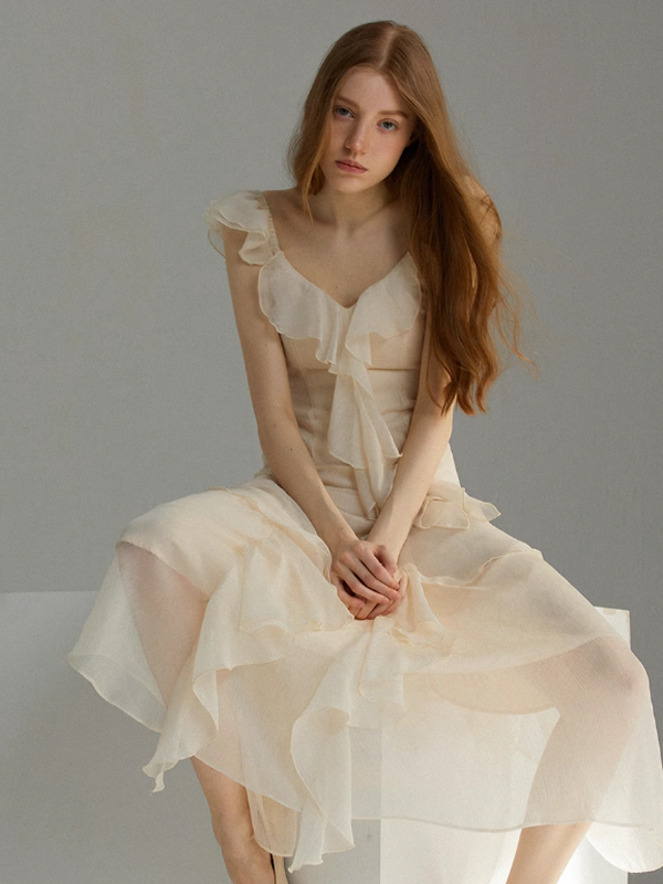 Ivory ruffle detail dress featuring a sheer layered skirt and feminine bow accent at the neckline, styled on a model sitting gracefully in a clean studio setting for a soft fairytale mood.