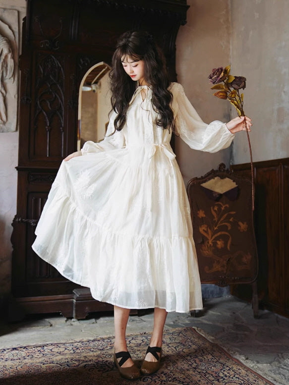Vintage fantasy dress aesthetic showing a model in a white embroidered dress, holding a dried flower and creating a romantic, fairytale-like mood.