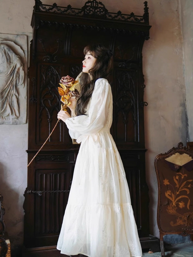 Woman in a fairytale white vintage dress holding a bouquet of dried roses, standing gracefully in front of an ornate wooden background.