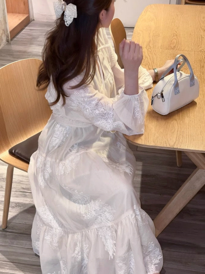 A woman sitting at a wooden table wearing a fairytale-inspired vintage dress with delicate white embroidery, expressing a soft fantasy aesthetic outfits style.