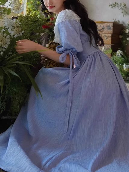 A fairytale-inspired vintage dress in soft blue, featuring a romantic white lace collar and ribbon-tied sleeves, styled in a dreamy floral room.
