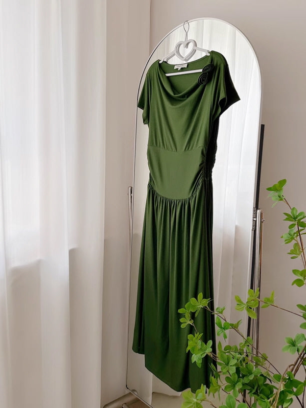 Forest green draped neckline midi dress with a flower brooch detail, hanging elegantly on a heart-shaped hanger in front of a full-length mirror. Soft natural lighting with a cozy indoor setting.