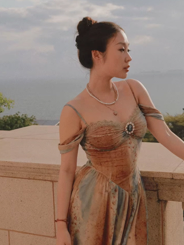 A vintage-inspired off-shoulder dress with lace detailing and a gemstone embellishment, exuding a princesscore aesthetic against a coastal backdrop