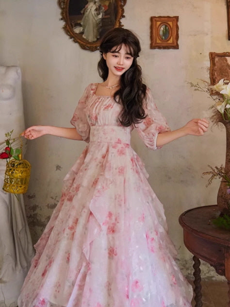 A vintage-style pink floral gown with puff sleeves and a flowing layered skirt, exuding a cottagecore charm in a whimsical setting.