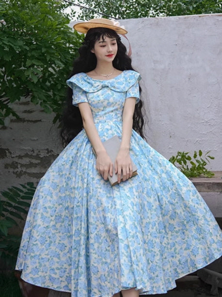 A charming blue floral dress with a wide collar and flowing skirt, styled with a straw hat and clutch for a vintage-inspired, fairytale look.