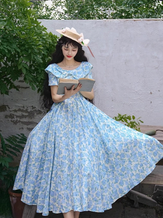 A fairytale-like blue floral gown with a twirl-worthy skirt, styled with a romantic straw hat and an open book for a whimsical cottagecore vibe.