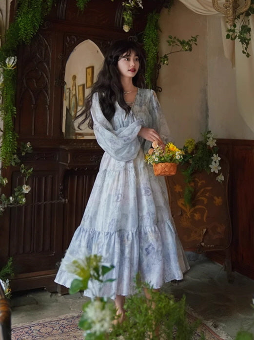 A soft blue floral dress with tiered ruffles and voluminous long sleeves, styled in a vintage-inspired indoor setting with a romantic, fairytale feel.