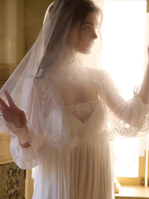 Backlit by golden sunlight, a woman lifts a lace-trimmed veil over her sheer white gown, creating a soft and ethereal fairycore silhouette.