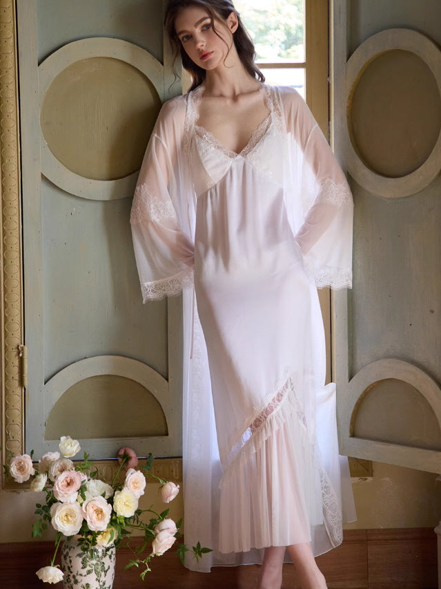 A woman in a vintage-inspired white robe and dress set with sheer lace sleeves stands gracefully by a painted wall, evoking a romantic fairycore mood.