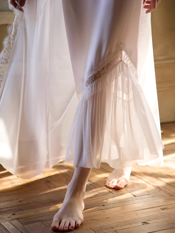 Close-up of the hemline of a flowing white nightgown with asymmetrical lace trim and pleated tulle, capturing soft cottagecore elegance in morning light.