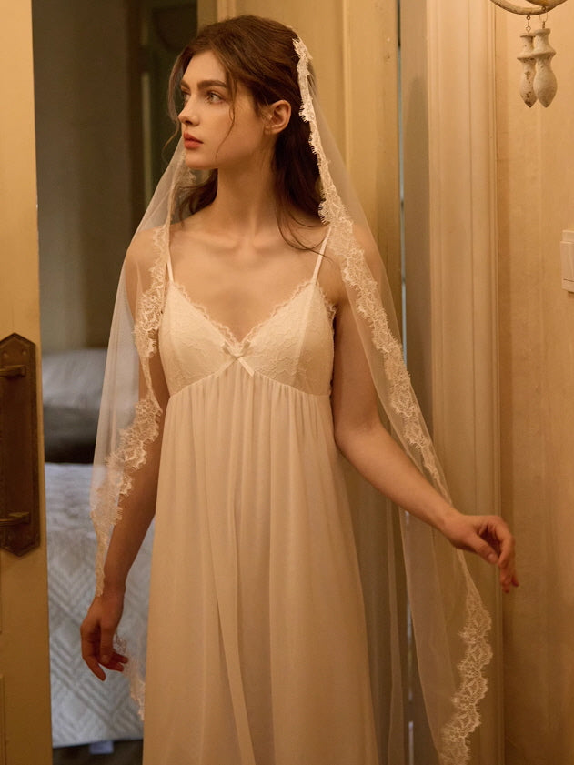 A model stands softly lit in a vintage hallway, wearing a flowy white slip dress with lace detailing, styled with a sheer robe in a princesscore aesthetic.