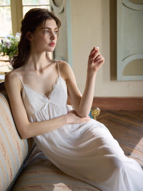 A model sits gracefully on a vintage sofa in a romantic white slip dress with lace details, styled in a serene and dreamy setting.