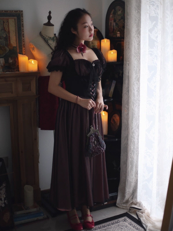 Model wearing a Romantic Fairytale dark romantic corset maxi dress with sheer puff sleeves, lace trim, and a lace-up bodice in a vintage coquette aesthetic outfit, styled in a candlelit room.